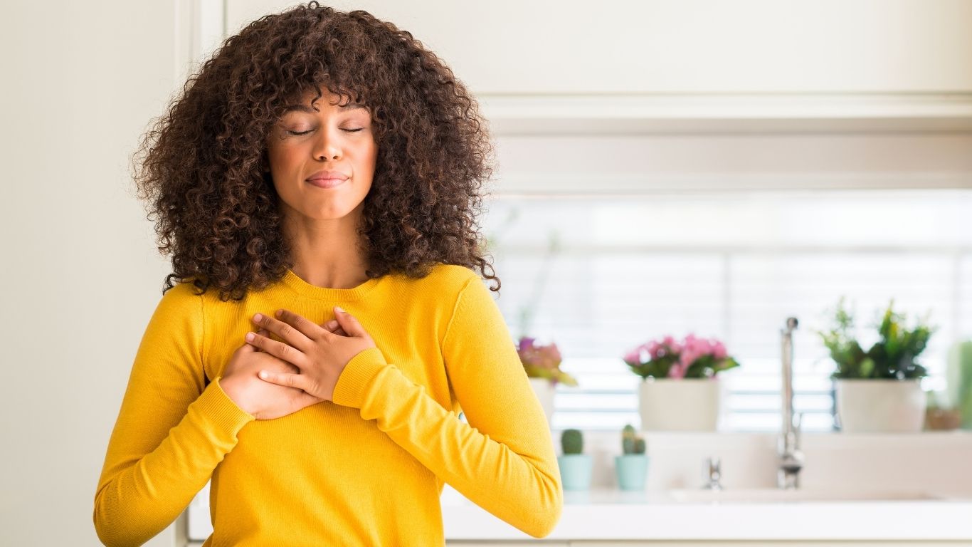Woman holding chest after Virtual RTT session with Scott E. Burgess, releasing emotional roadblocks and experiencing deep relief and transformation.